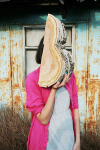 Woman holding wood while standing against wall