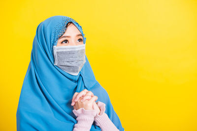 Young woman wearing mask against yellow background