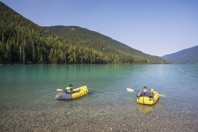 Two young boys learning how to paddle kayak on scenic lake.