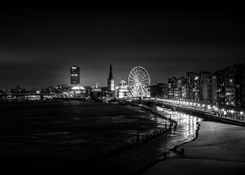 Illuminated ferris wheel by city against sky at night