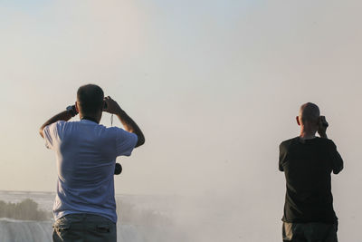 Rear view of men at niagara falls against sky