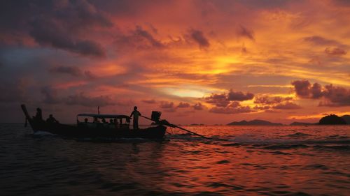 Silhouette people in boat on sea against orange sky