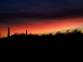 Silhouette of factory against sky at sunset
