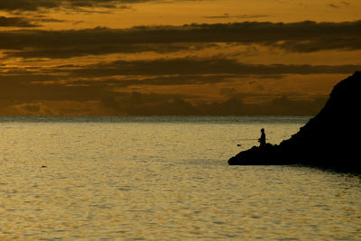 Silhouette man fishing in sea against sky during sunset