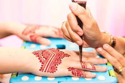 Cropped image of beautician masking henna tattoo on bride hand during wedding