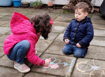 Brother and sister are drawing with chalk in the backyard