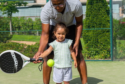 Rear view of boy playing with ball on tennis court