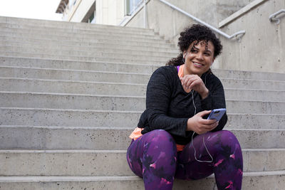 Low angle view of woman listening music through mobile phone while sitting on steps