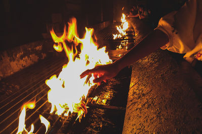 Cropped hand of woman reaching towards flame at night