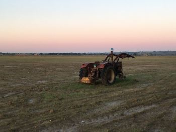 Tractor on field against sky during sunset