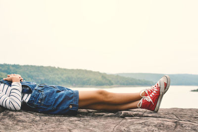 Low section of woman lying on rock by lake against sky