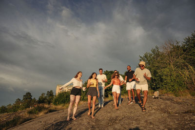 Multiracial male and female friends dancing while moving down on rock against sky