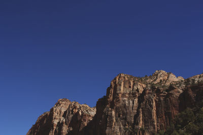 Low angle view of rocky mountains against clear blue sky