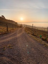 Road amidst field against sky during sunset