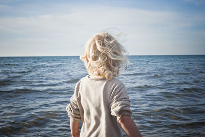 Rear view of boy standing in sea against sky