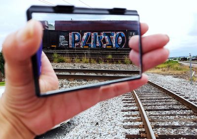 Close-up of hand on railroad track against sky