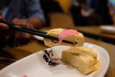 Midsection of man holding tamagoyaki with chopsticks over table