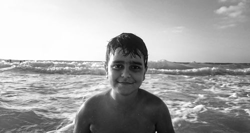 Close-up portrait of shirtless boy in sea against sky