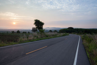 Road by trees against sky during sunset