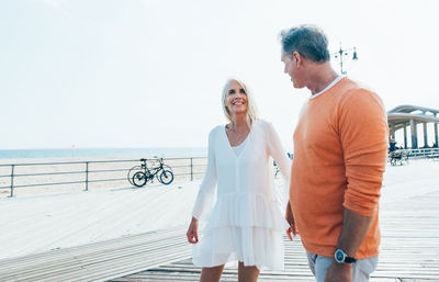 Smiling couple holding hands while standing on promenade by beach