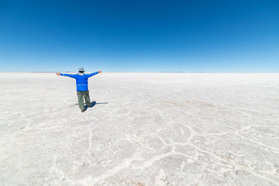 Full length of man walking in desert against clear blue sky