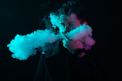 Portrait of man smoking electronic cigarette against black background