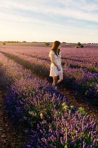 Full length of woman with flowers on field against sky during sunset