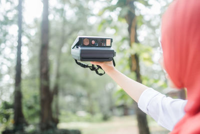 Midsection of person photographing camera in forest