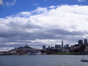 City at waterfront against cloudy sky
