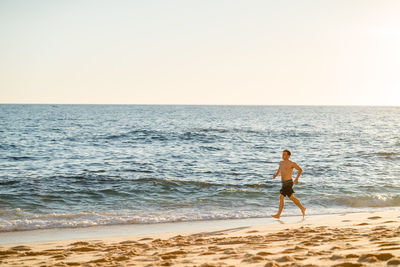 Shirtless man walking on shore at beach