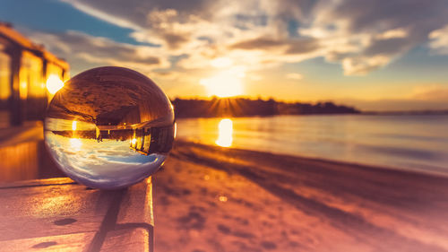 Close-up of glass on beach against sky during sunset