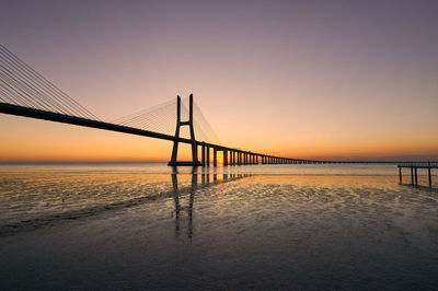 Bridge over calm sea against sky during sunset