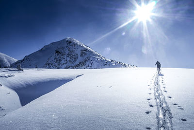 Rear view of man hiking on snow against sky