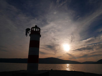 Lighthouse by sea against sky during sunset