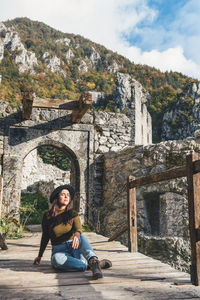 Young woman sitting on footbridge of old castle ruin, autumn, fall, earth tones, style.