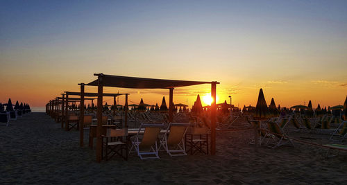 Chairs on beach against sky during sunset