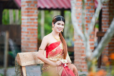 Portrait of smiling young woman wearing traditional clothing and jewelry while sitting outdoors