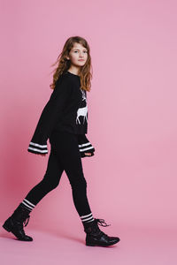 Portrait of young woman standing against pink background