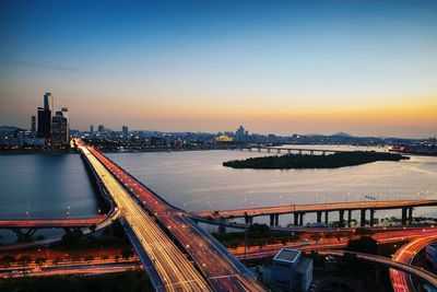 High angle view of light trails on bridges by river in city during sunset