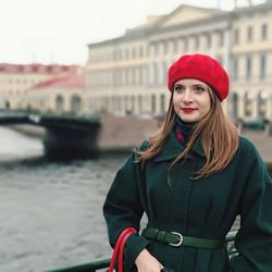 Young woman wearing warm clothing while looking away in city by canal
