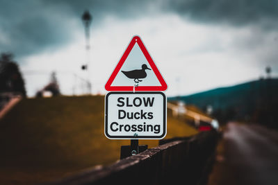 Bokeh of a road sign warning to watch out for ducks and ducklings crossing the road, over a fence