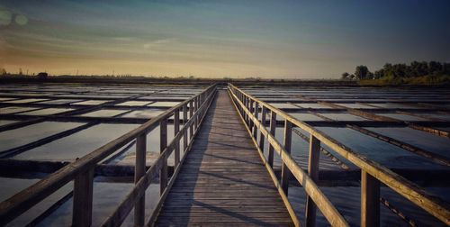 Boardwalk on landscape against sky during sunset