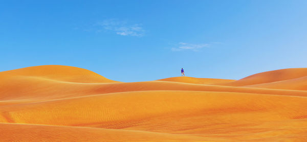 Mid distance view of man standing at desert against blue sky