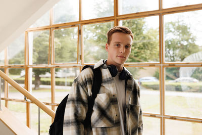 Portrait of young man standing against window