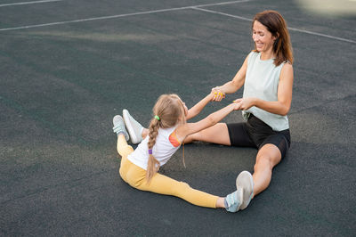 Mother and daughter exercising while sitting on footpath