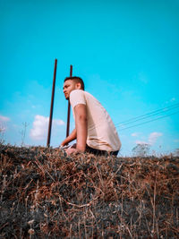 Low section of man sitting on field against sky