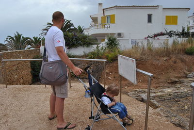 Man with son sitting in baby stroller against house