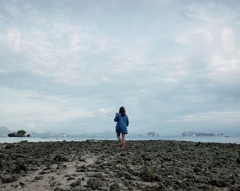 Rear view of woman standing on beach against sky