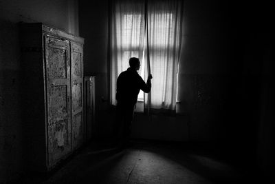 Silhouette man standing by window in darkroom
