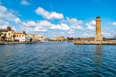 Buildings by sea against cloudy sky